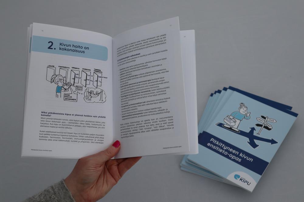 Ensitieto-oppaita pinossa. Avattuna sivu, jonka otsikkona on Kivun hoito on kokonaisuus.