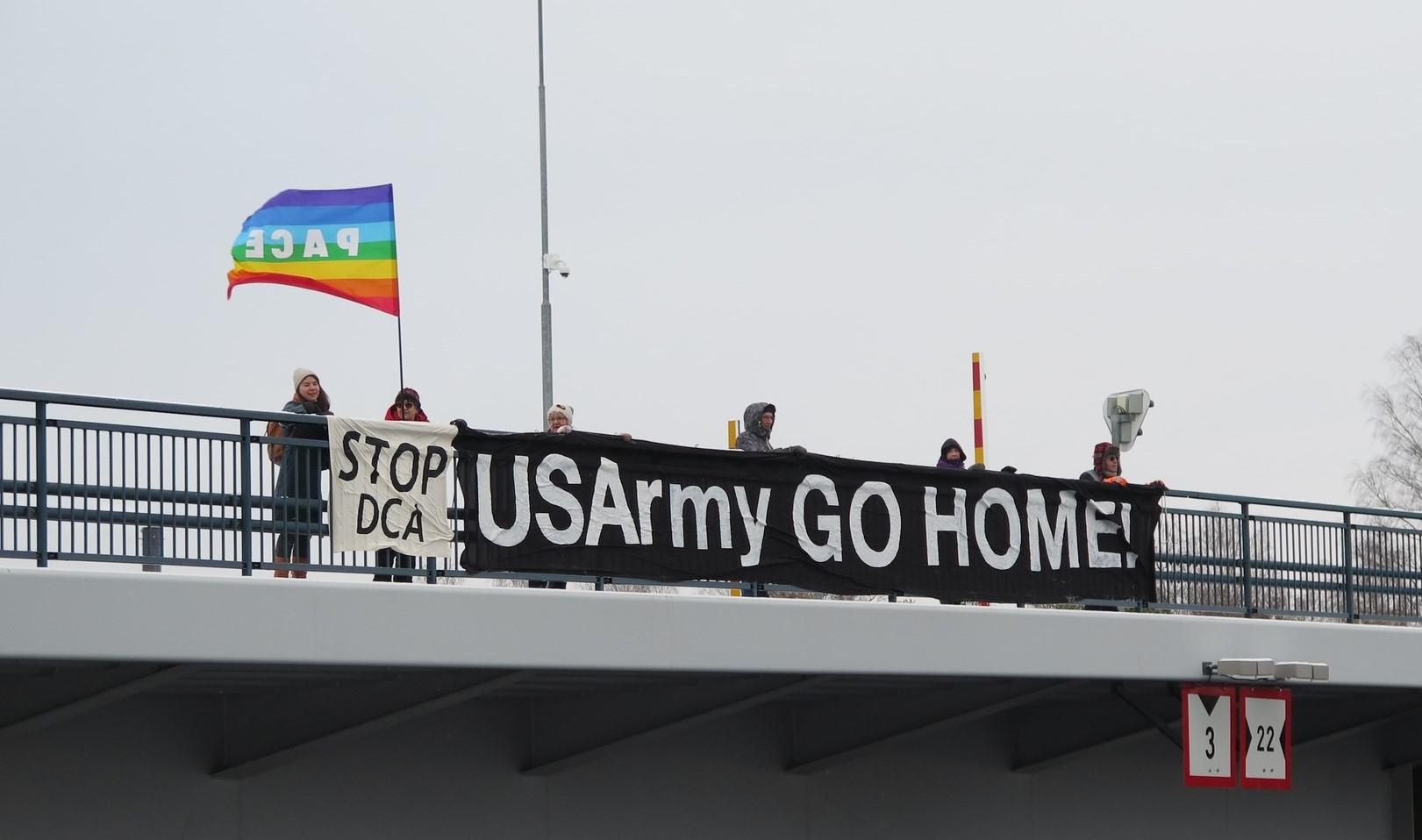 Mielenosoittajia sillalla pitämässä sillankaikeella näkyvää "US Army Go Home!" -banderollia sekä kädessä rauhanlippua.