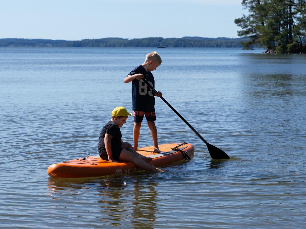 Kaksi poikaa sup-laudalla. Toinen istuu ja toinen meloo seisten.