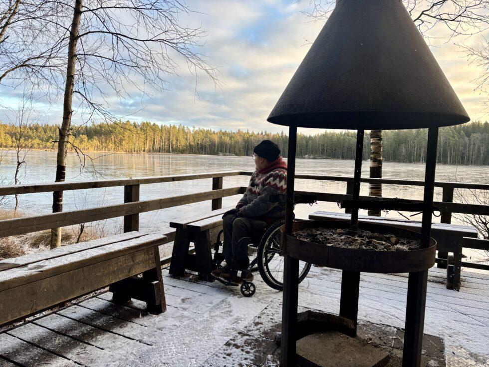 Laavu järven rannalla. Etualalla nuotiopaikka, jonka takana Niko pyörätuolissa.