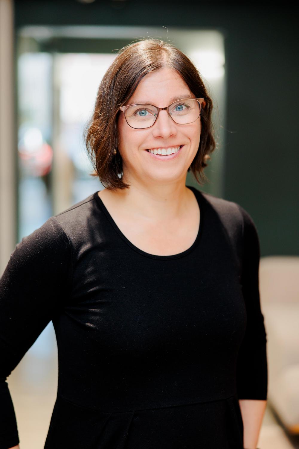 Nainen mustassa paidassa ja ruskeissa silmälaseissa.