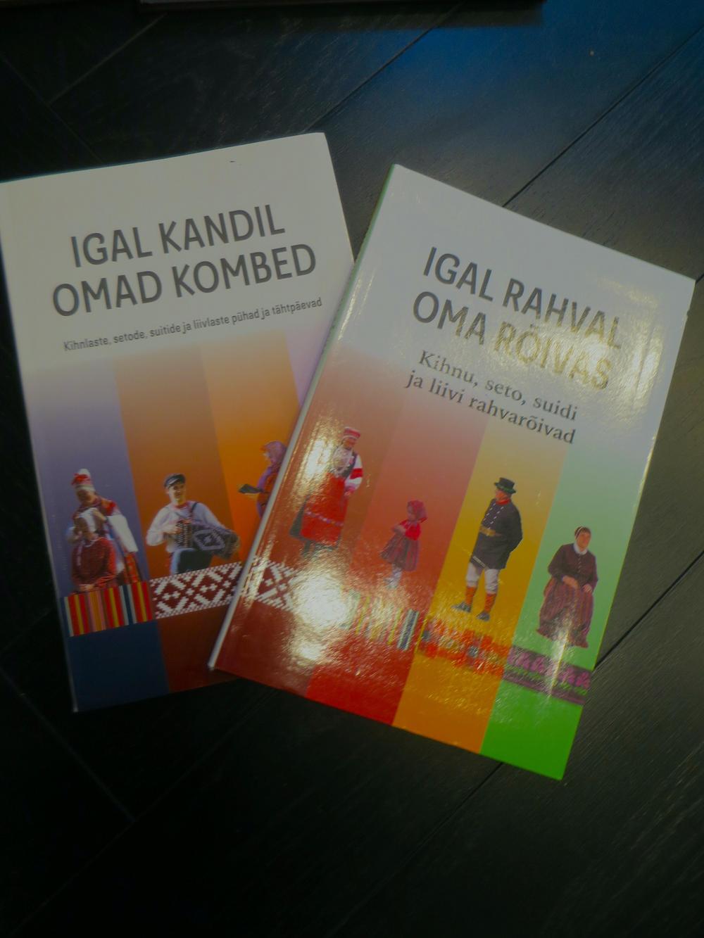 Nämä kaksi kirjaa esittelevät kihnulaisten, setojen, suitien ja liiviläisten kansallispukuja ja kansankalenterin juhlapäiviä. Kuva: Tapio Mäkeläinen, 2024.