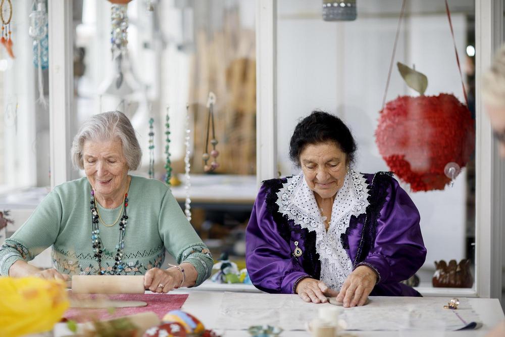Kvinnorna sitter bredvid varandra och arbetar med lera. Orvokki bär en traditionell romsk dräkt. 