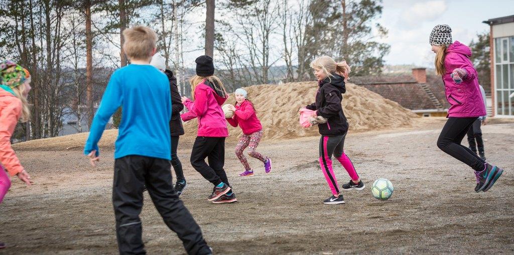 Koululaisia pelaamassa jalkapalloa koulun pihalla