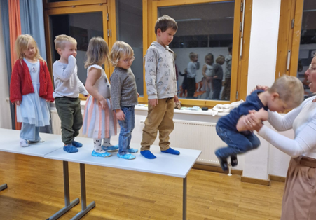 Lapsia hyppäämässä pöydältä alas aikuisen avustamana.