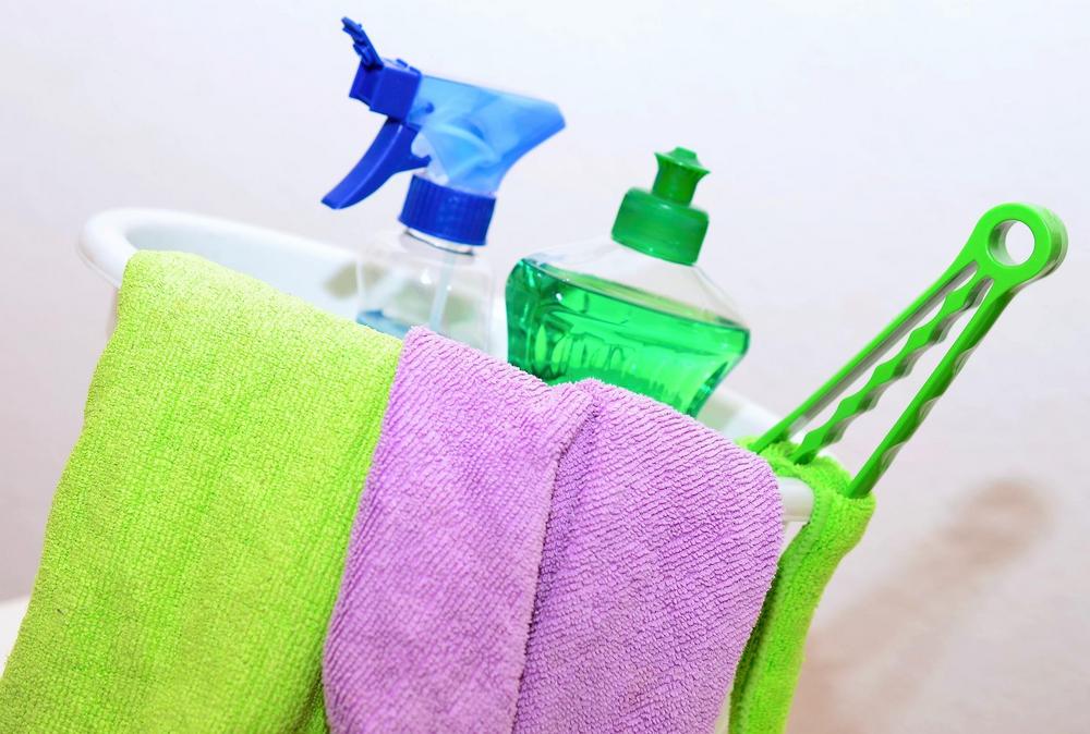 Kuvassa on siivousämpäri, jossa on suihkepullo, pesuainepullo sekä vihreä ja vaaleanpunainen mikrokuituliina.