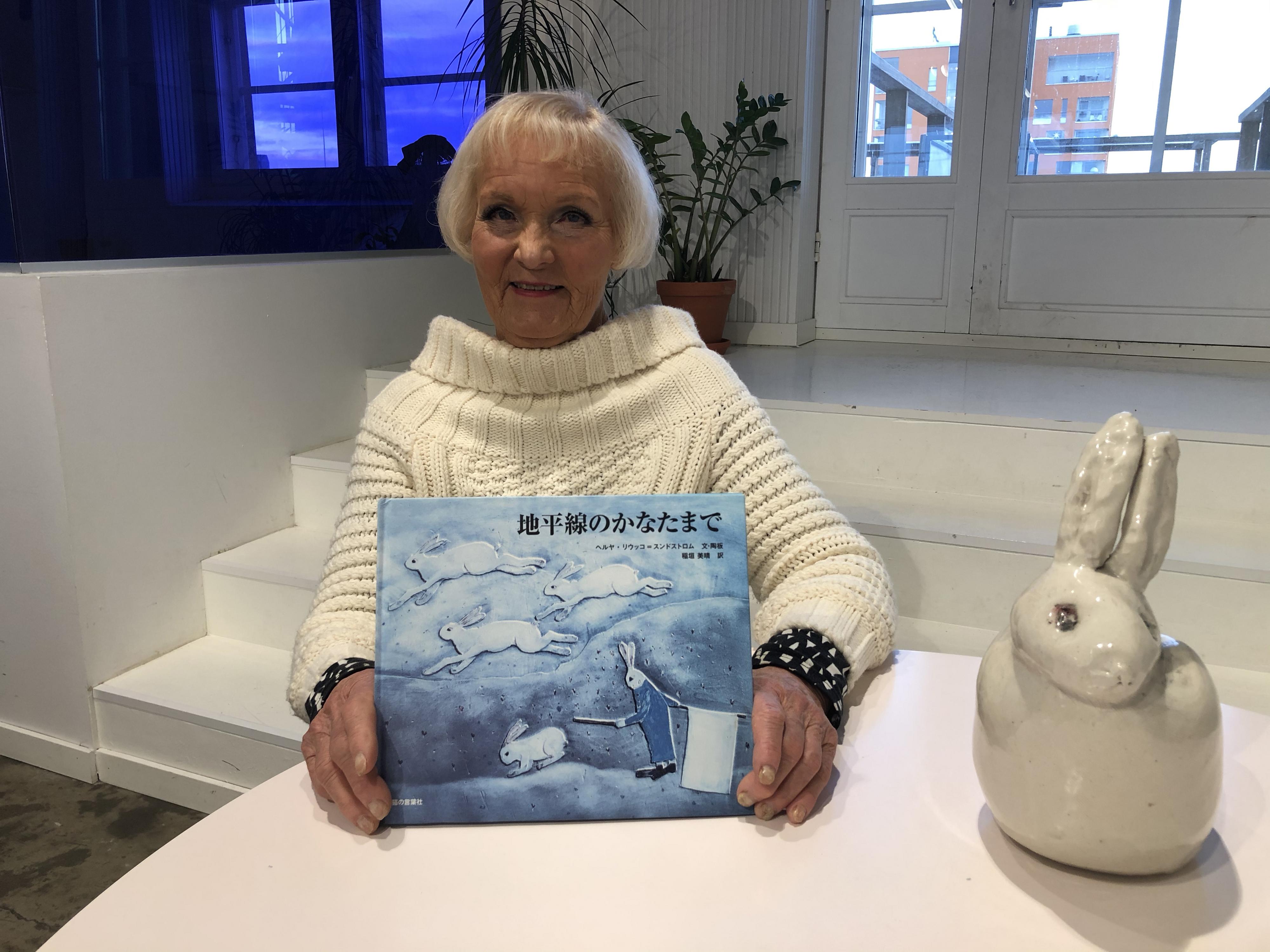 Kuvassa professori Heljä Liukko-Sundström pitelee Jäniksenpoika-teoksen japaninkielistä laitosta vieressään tarinaan liittyvä keraaminen jänisveistos.