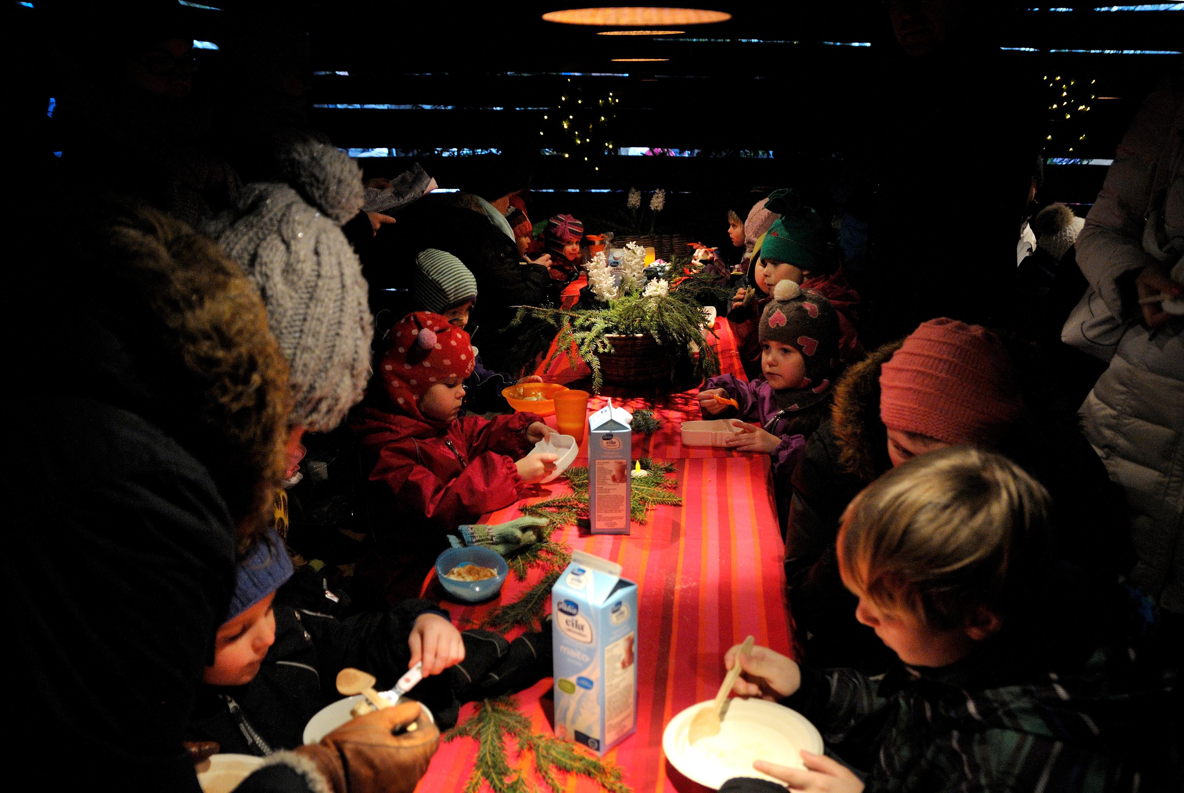 Kuvassa lapsia ja aikuisia istumassa Antin kaffeliiterissä pöydän ääressä. Lapset syövät puuroa.