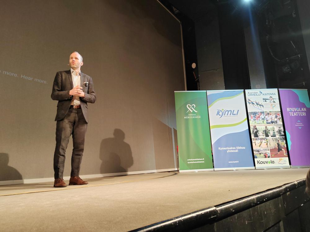 Kuvassa ministeri Poutala seisoo teatterin lavalla puhumassa