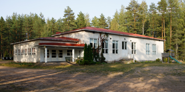 Vaalea kivitalo havupuiden ympäröimänä.