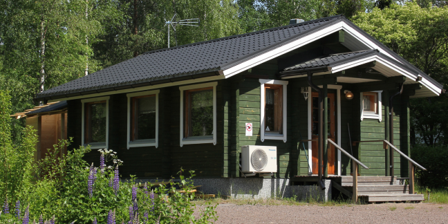 Pieni, vihreä hirsimökki vehreiden puiden ympäröimänä.