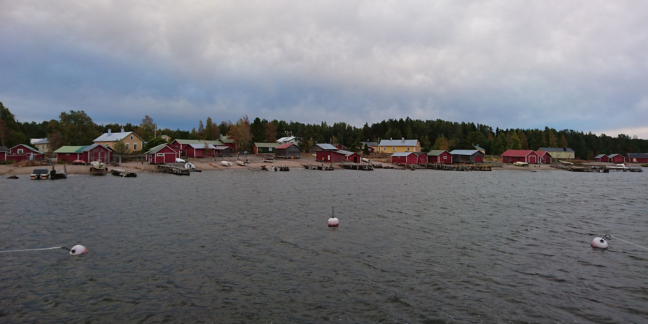 Tumma taivas ja merimaisema, jossa näkyy rivi taloja saarella.