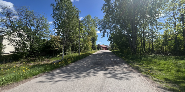 Kesäinen vehreä tie, jonka päädyssä punainen rakennus.
