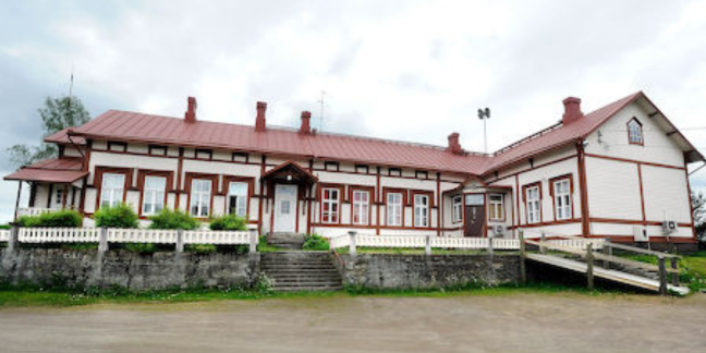 Suuri valkea puutalo, jossa punaiset ikkunanpielet ja katto. 