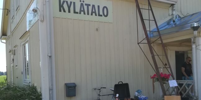 Vaalea puinen kylätalo, jossa kyltti "kylätalo".
