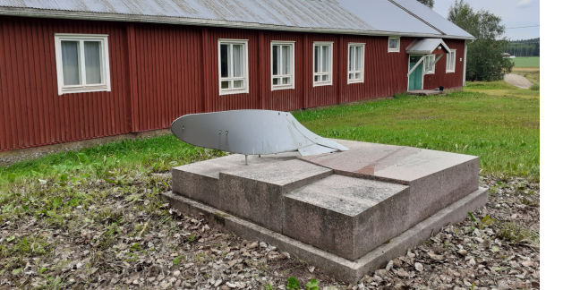 Punamultainen rakennus, jonka edustalla kivinen veistos.