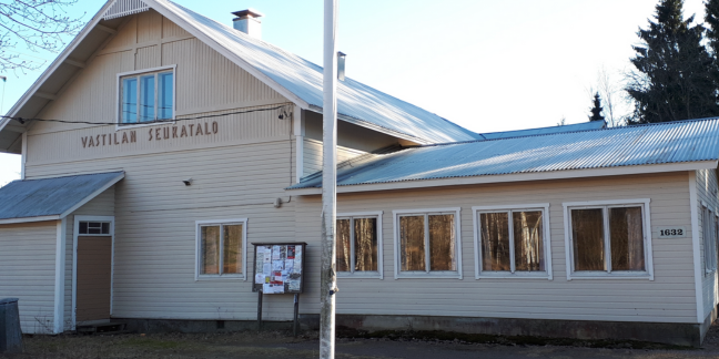 Vaalea suuri hirsitalo, jonka seinällä kyltti "Vastilan seurantalo".