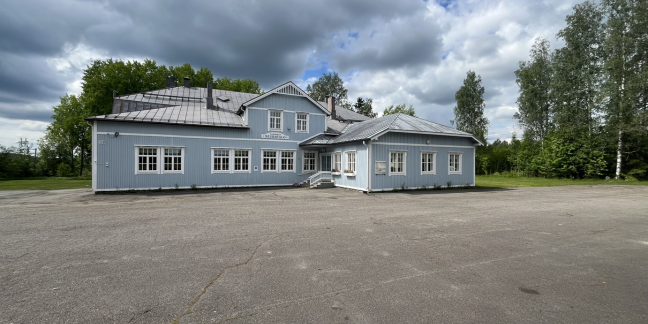 Suuri, vaaleansininen puinen rakennus, jonka ympärillä lehtipuita.