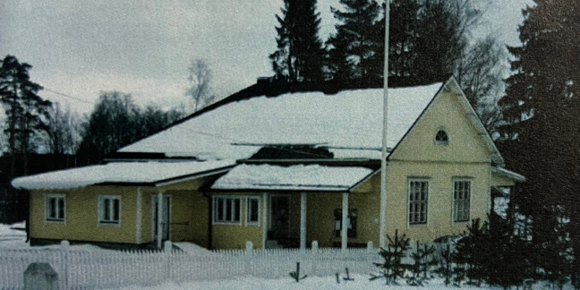 Keltainen puutalo lumisessa maisemassa.