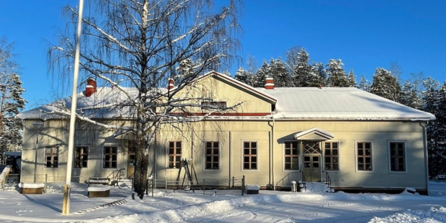 Suuri vaaleankeltainen puutalo kirkkaassa talvisessa maisemassa. 