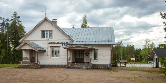 Aitomäen nuorisoseurantalo, vaalea, suuri puutalo, jonka ympärillä hiekkakenttää ja havupuita.
