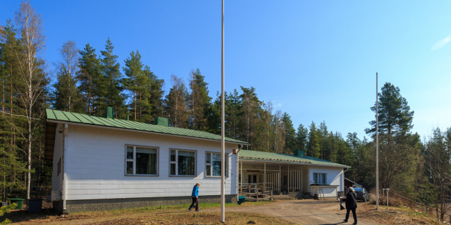 Puutalo, jossa vihreä katto ja valkoiset seinät metsän ympäröimänä.