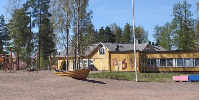 Keltainen puutalo hiekkakentän takana.