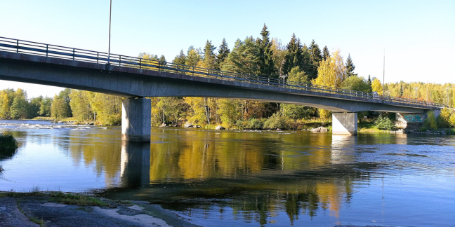 Jokea halkova silta, jonka taustalla syyskesäinen metsämaisema.