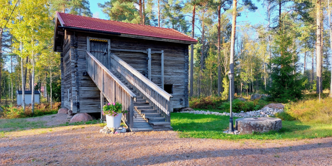 Hirsinen, kaksikerroksinen talo, havumetsän kupeessa.