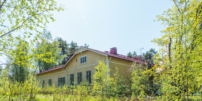 Suuri keltainen hirsitalo vaaleanvihreän keväisen luonnon ympäröimänä.