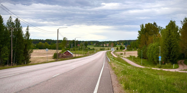 Tyhjä asfalttitie kesäisessä maisemassa, tien molemmin puolin peltoa ja lato.