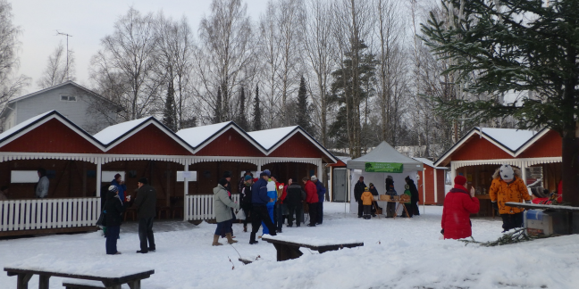 Pieniä punavalkoisia myyntikojuja talvisella, lumisella torilla.