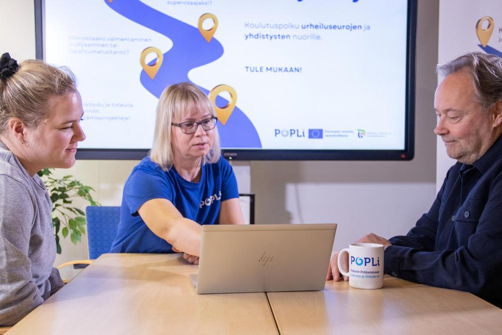 Kuvassa kolme ihmistä pöydän ääressä.