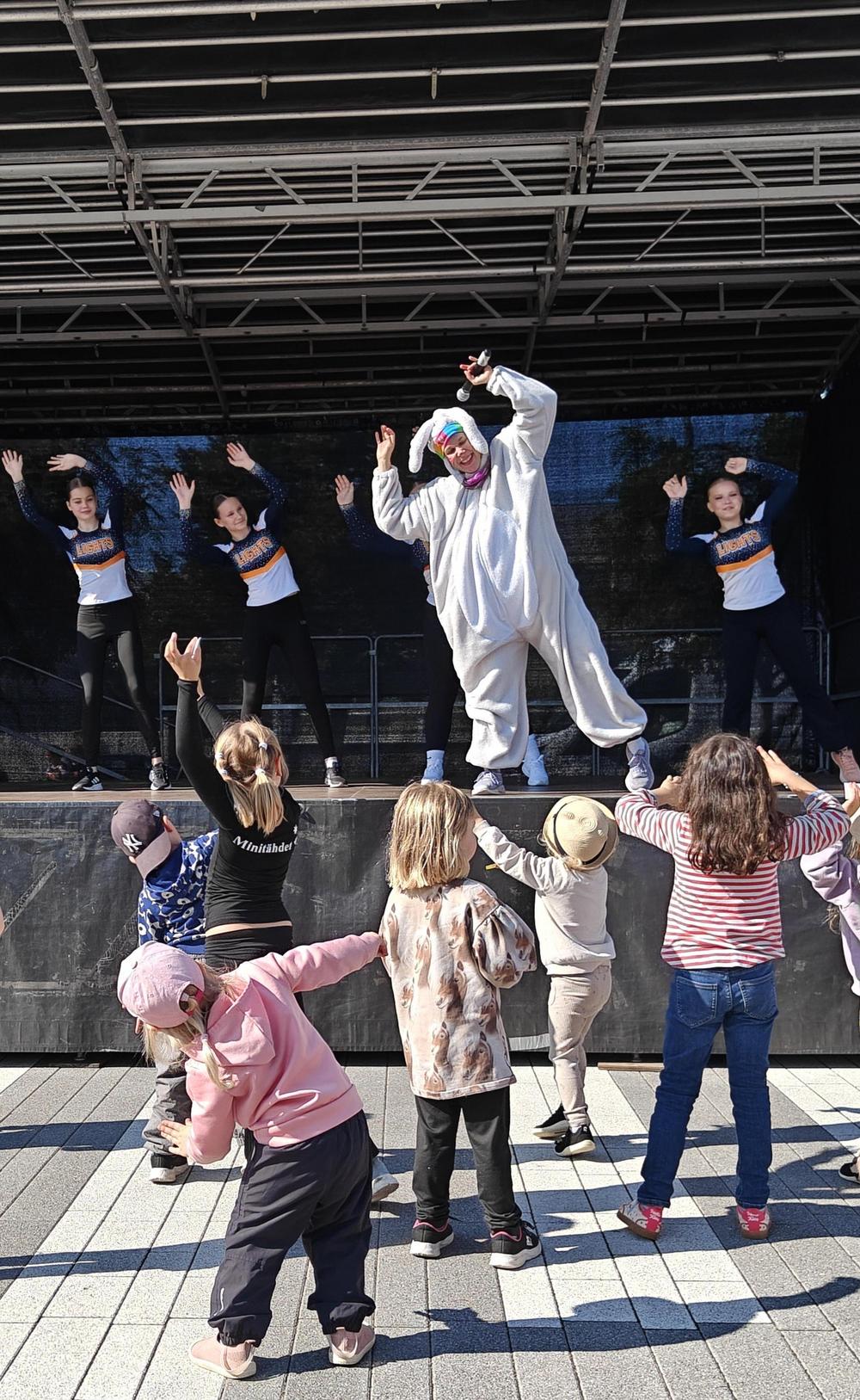 Jekku-jänö ja Northernlights cheerleading urheilijoita lavalla. Edessä pieniä lapsia osallistumassa liikkeisiin.
