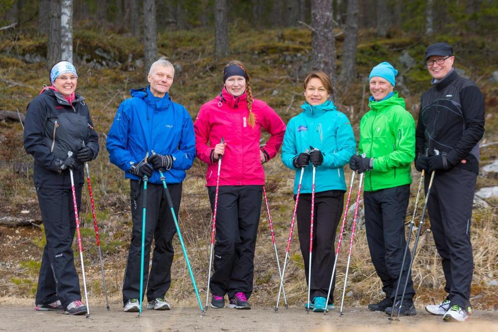 Ryhmä ihmisiä seisoo ulkona metsäisessä ympäristössä ja pitää käsissään sauvakävelysauvoja.