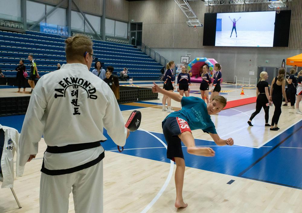 12-vuotias Topias Järvenpää potkaisee Ouluhallissa harjoituspadiin, jota pitelee taekwondoseuran harrastaja.