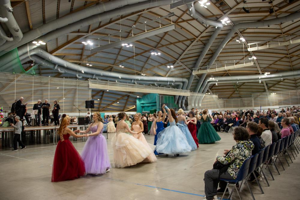 Juhlapukuihin pukeutuneet tanssijat esiintyvät tapahtumahallissa yleisölle.