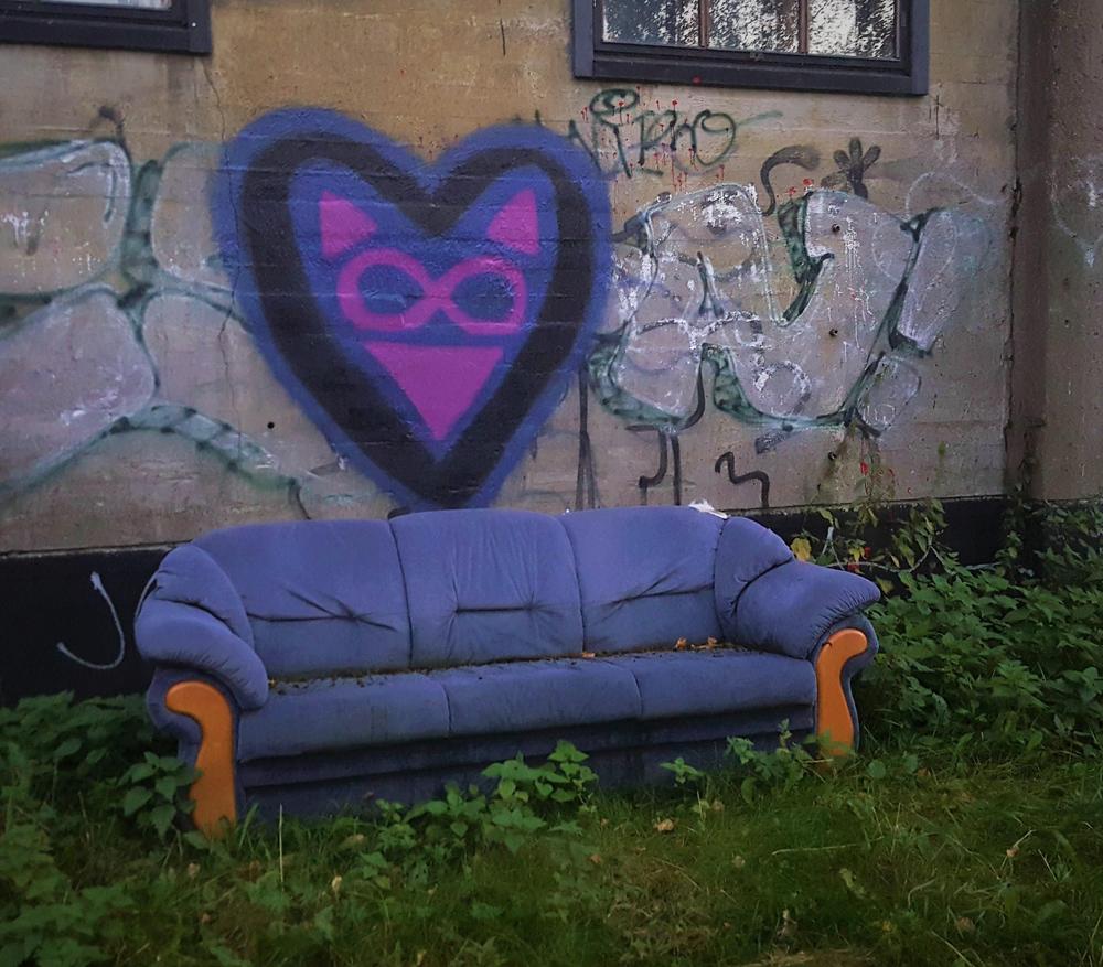 Sininen sohva ulkona graffiteilla maalatun seinän edustalla. Sohvan taakse on maalattu suuri violetti-musta sydän.