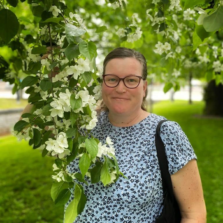 Nainen hymyilee kukkivan omenapuun alla