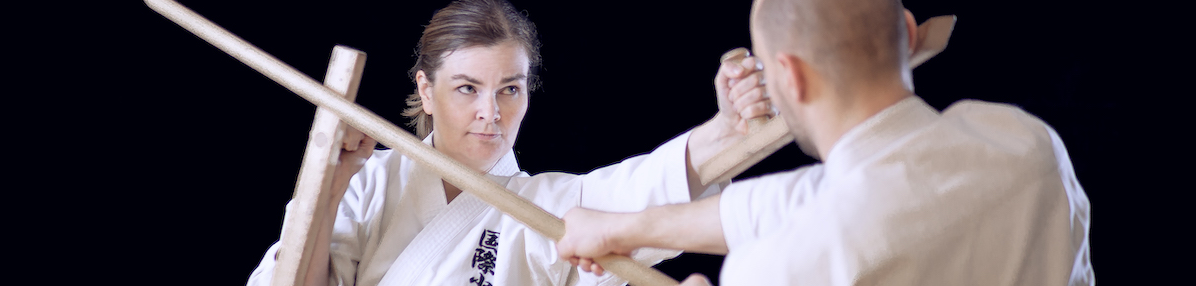 Two karatekas practice kobudo with Japanese wooden weapons.