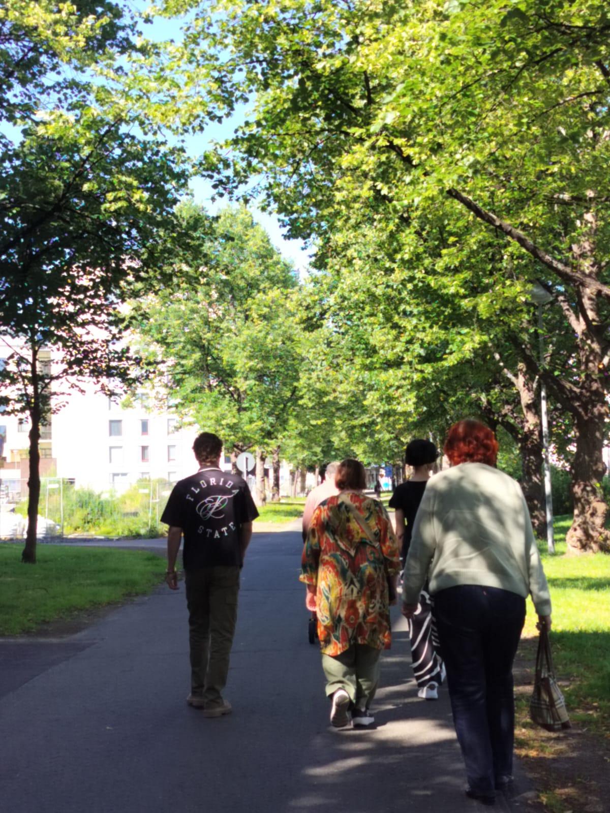 Ihmiset kävelevät puiden reunustamalla kevyenliikenteenväylälllä.