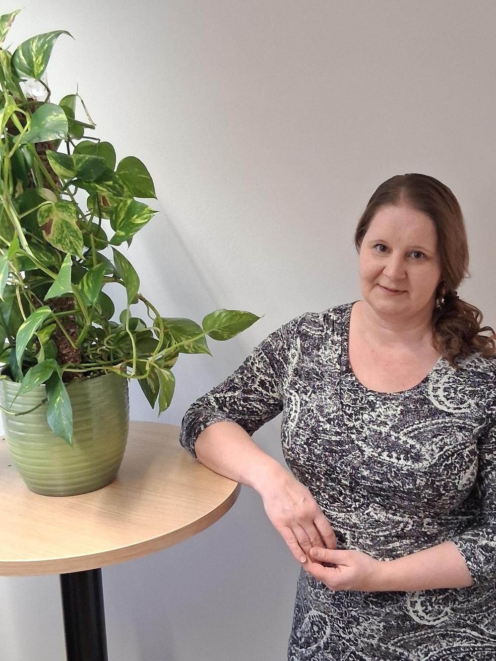 Merja-Kaija-seisoo-nojaten-kyynerpäällään-pöytään-jolla-on-viherkasvi