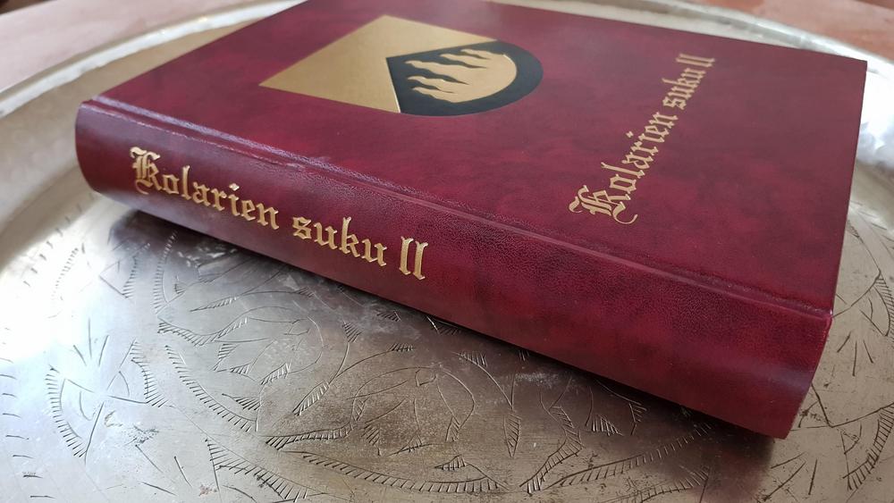 Punakantinen Kolarien Suku II-kirja hopenvärisellä vadilla. Kirjan kannessa kultavärillä Kolareiden vaakuna.