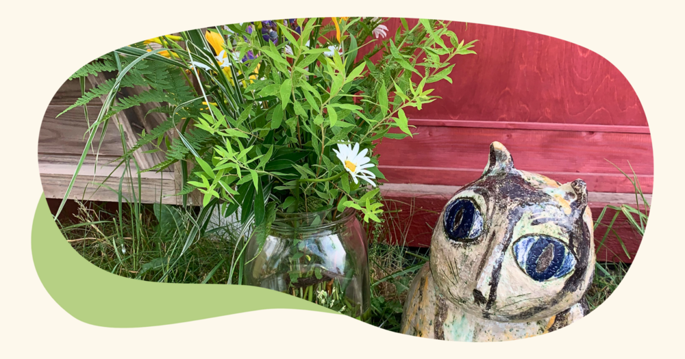 En keramisk kattstaty och en glasvas med vilda blommor.