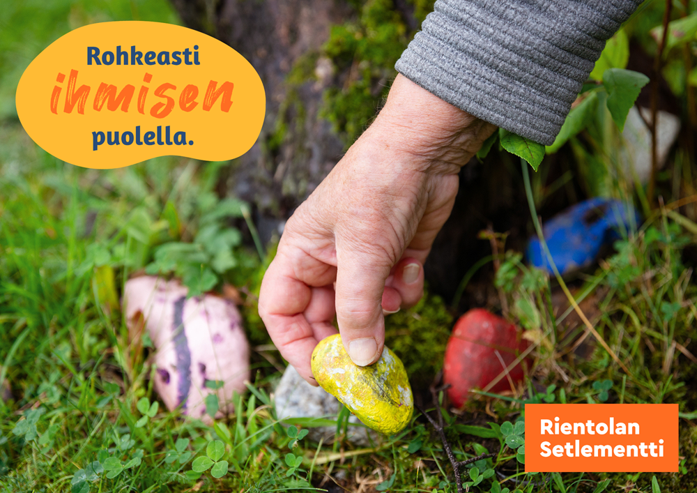 Kuva värillisestä kivestä, jota ihmisen käsi nostaa maasta ja pitää kädellään luonnossa.