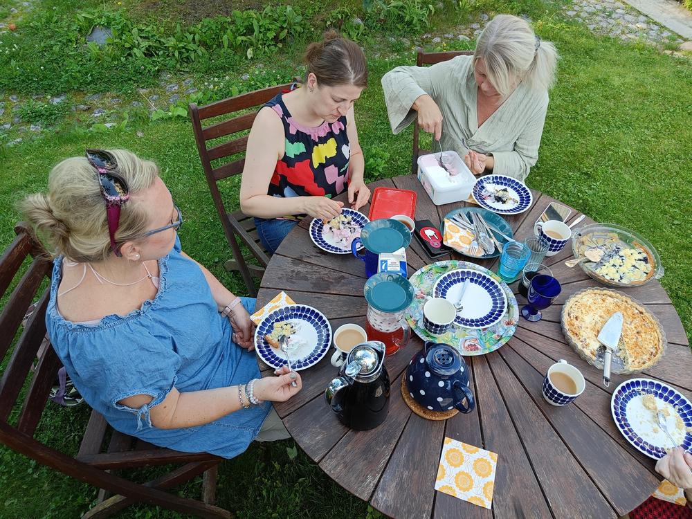 Neljä naisoletettua pyöreän puutarhapöydän ääressä, kuva otettu yläviistosta. 