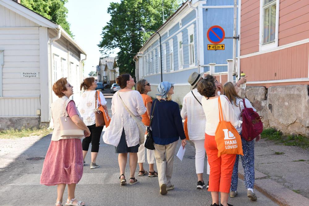 A group is walking on the old town area on the street Kuningattarenkatu. They are admiring colorful old treehouses from 1800´s.