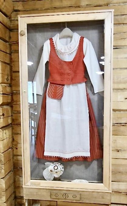 Vitriinissä on esillä punavalkoinen Hattulan naisen kansallispuku ja siihen kuuluva valkoinen kirjailtu trykkimyssy.