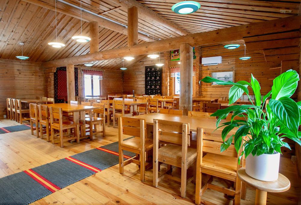 Hirsistä rakennetun Hattula-Pirtin sali, jossa on pöytiä ja niiden ympärillä tuolit sekä etualalla sivupöydällä vehreä vehka-kasvi.