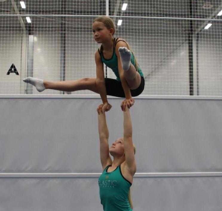 Kuvassa on kaksi nuorta, joista toinen kannattelee toista suorien käsiensä päällä, samalla kun toinen suorittaa käsien päällä nostoliikkeen nimeltä haarakulmapito.